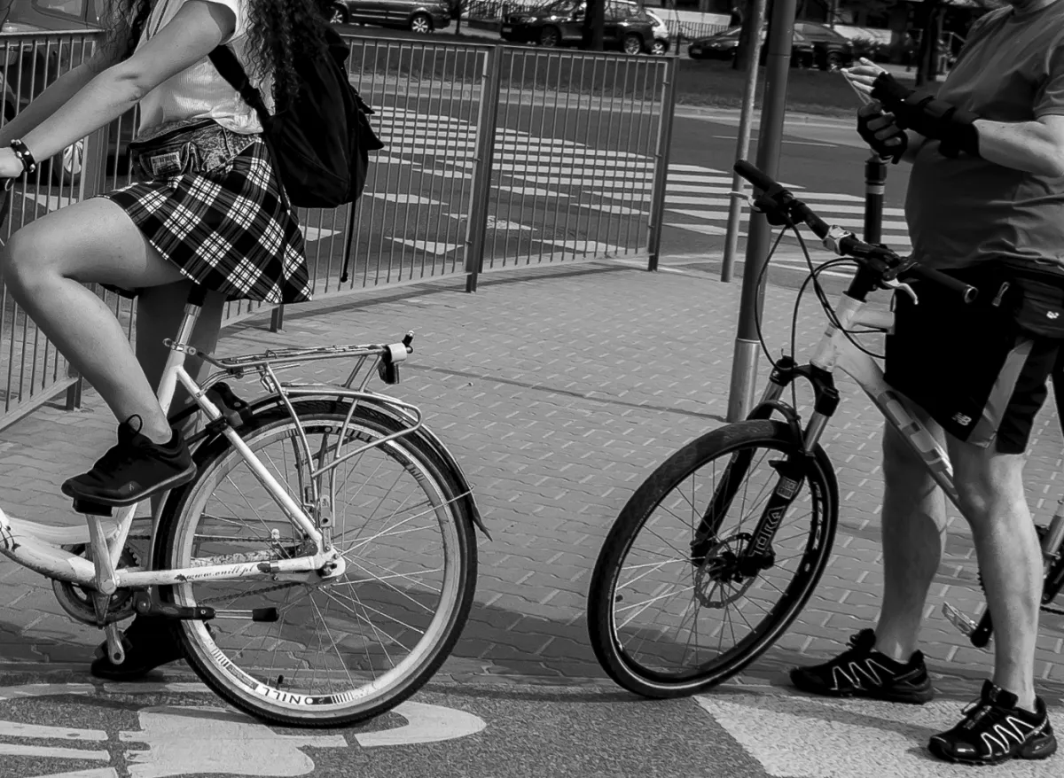 Man checking his phone beside bicycles and a rider in a black skirt
